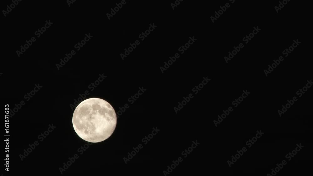 Wall mural time lapse of bright full moon passing through night sky then fading to black as clouds fill frame.