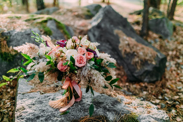 Beautiful wedding bouquet lying on a stone in the park. Autumn wedding