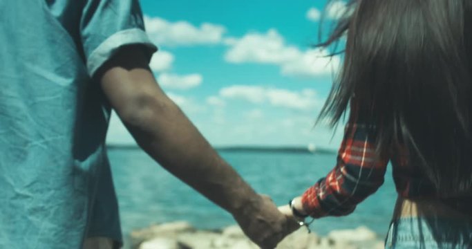 Young adult interracial couple on a beach, Caucasian female and African American man in casual clothes enjoying summer day on a sea shore. 4K UHD 60 FPS SLO MO