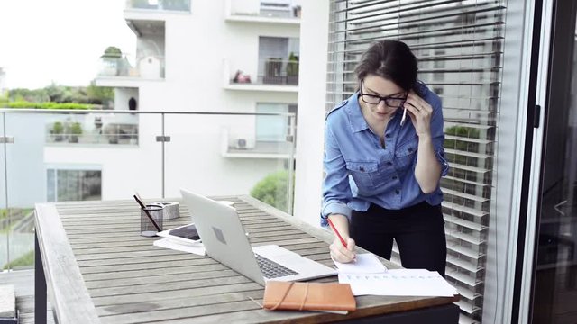 Woman on balcony working from home, making phone call.