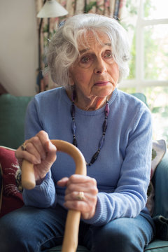 Sad Senior Woman Sitting In Chair Holding Walking Cane
