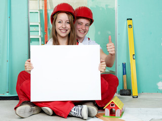 Young couple with white board in a building lot 
