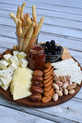Cheese plates served with grissini, crackers, dates, jam, olives and nuts on wooden background