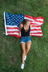 Young caucasic american woman resting on grass with american flag