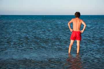 Slim guy posing in red swimwear in sea water