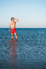 Slim guy posing in red swimwear in sea water