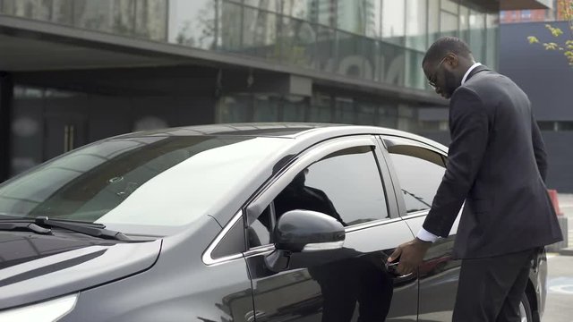 Scrupulous Afro-American man wiping his new car before leaving parking lot