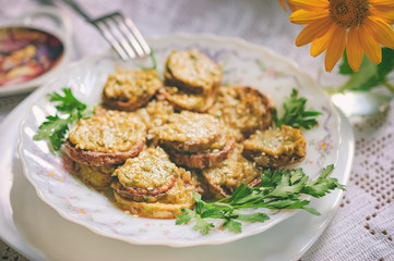 Rustic dinner with fried zucchini slices with nut sauce and greens. A white plate with food stands on a lacy rustic tablecloth, a bouquet with flowers in the background. Selective focus