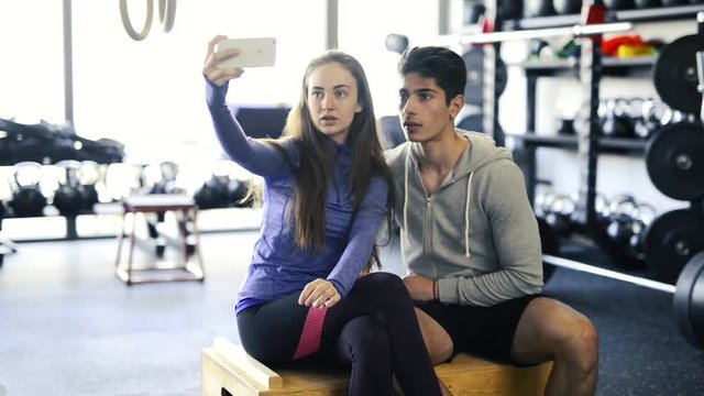 Fit couple in crossfit gym taking selfie with smartphone.