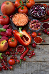 composition of red vegetarian products: fruits, vegetables, spices and beans on wooden background. Apple tomatoes, currant peppers, raspberries cherry, lentils. Healthy food. Copy space for text