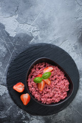 Stone slate tray with a bowl of strawberry risotto, above view over grey stone background with space, vertical shot