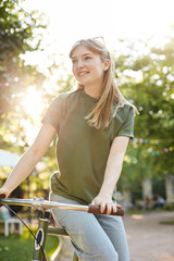 Girl sitting on a bike. Portrait of young woman in city park riding a bycicle looking off camera wearing shades on a sunny summer evening. Hipster lifestyle concept.
