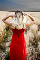 Beautiful blond woman in a red dress, on a wheat field at sunset