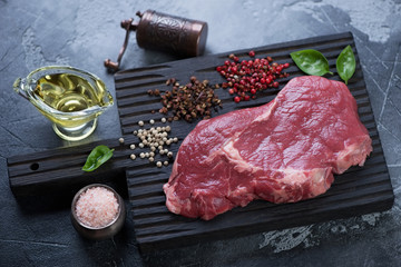 Black wooden chopping board with fresh uncooked ribeye steak and seasonings, studio shot