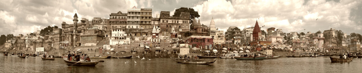 Fototapeta na wymiar Varanasi, India - November 2009: Boats with tourists and locals floating along the embankment, ghats and ancient buildings.