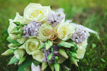 Beautiful bridal bouquet of bride on green grass with gold rings