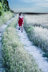 Beautiful blond woman in a red dress on a path in the wheat field at sunset