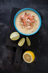 Black wooden serving board with a bowl of potato and shrimps cream-soup, high angle view on a dark scratched metal background