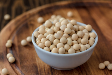 Organic soybeans at white ceramic bowl over wooden table.