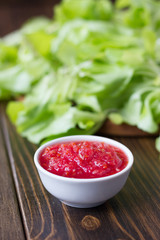 Mexican salsa or indian chutney in white ceramic bowl against green herbs