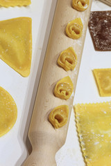 Fresh italian pasta of many sizes with wooden rolling pin