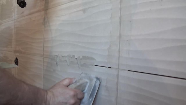 Worker putting fugue on the wall in the kitchen. Tile grouting
