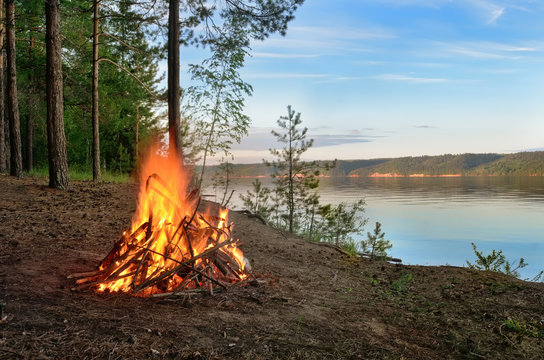 Big Night Bonfire On The Riverbank In The Forest Clearing, Flames, Sparks And Fireplace.