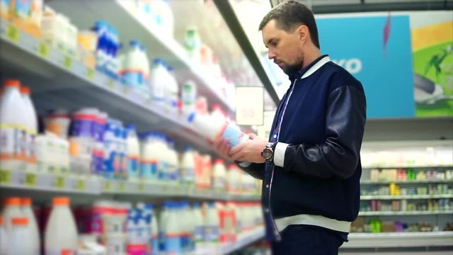 An adult man chooses a package of milk in the dairy department of a grocery store, people see plastic cans with pasteurized milk for breakfast