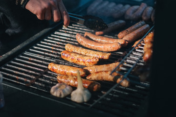 Sausages cooked at barbecue outdoors with chefs hands out of focus. Street food, fast food