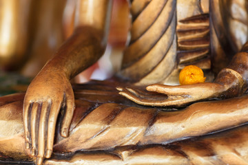 Gilded hand of Buddha holding flower, close up of temple statue from Thailand