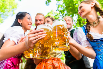 Freunde, zwei Männer, drei Frauen, stehen im Biergarten mit Maßkrügen