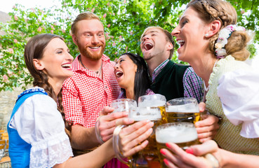 Fünf Freunde, Männer und Frauen, haben Spass in Biergarten beim Anstoßen mit Maßkrügen