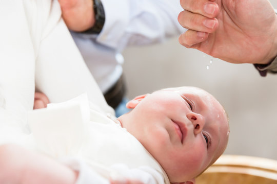 Baby weint bei der Taufe als der Pfarrer Weihwasser auf seinen Kopf tr&auml;ufelt