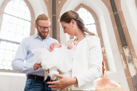 Junge Eltern mit ihrem Baby im Taufkleid in einer Kirche
