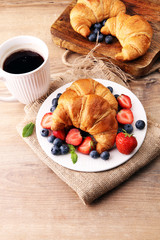 Delicious breakfast with fresh croissants, coffee and ripe berries on old wooden background