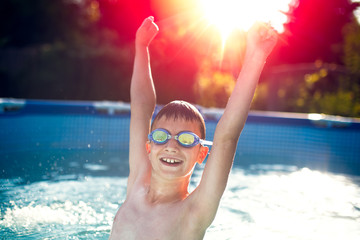 Happy kid enjoying summer sunset in swimming pool in sunset, hands up in the air