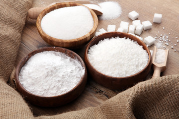 Bowl and scoop with white sand and lump sugar on brown wooden background