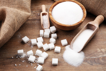 Bowl and scoop with white sand and lump sugar on brown wooden background