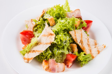 salad with bacon, tomatoes and croutons on a white plate (close)