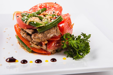 meat salad, tomato decoration on a white plate on a light background