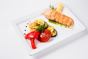 Healthy food, red fish, vegetables, herbs, lemon on a white plate and a white background
