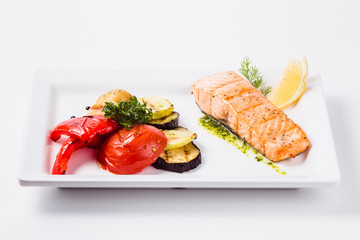 Healthy food, red fish, vegetables, herbs, lemon on a white plate and a white background
