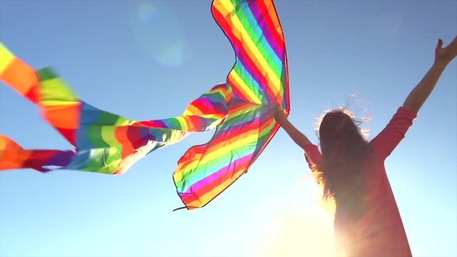 Beautiful young woman with flying colorful kite over clear blue sky and shining sun. Freedom concept. Slow motion 240 fps. 4K UHD video 3840X2160