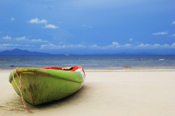 Travel to island Phi Phi, Thailand. The old green-red-white boat on the sand beach with sea and a mountain and blue sky on background.