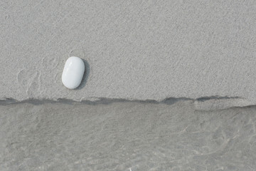 White pebbles, round small stones in a row on the wave line on white sand beach, space for letters or text