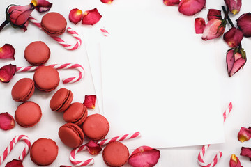 white background with petals of red roses, macaroons and caramel sticks;