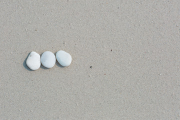 Fototapeta na wymiar White pebbles, round small stones in a row on a wet white sand beach, space for letters or text
