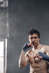Strong boxer in the rays of the sun and smoke training hands with boxing wraps. Boxer putting on straps preparing for combat on a dark background.