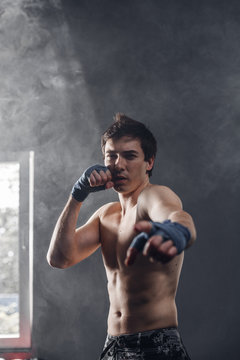 Boxer in the sun and smoke training hands with boxing wraps. Muscular strong man on background boxing gym.