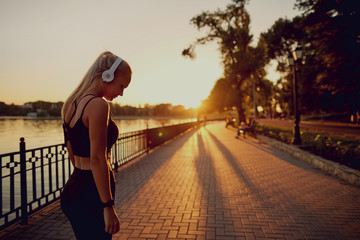 The concept of a healthy lifestyle. Girl in headphones on a run the park at sunset.